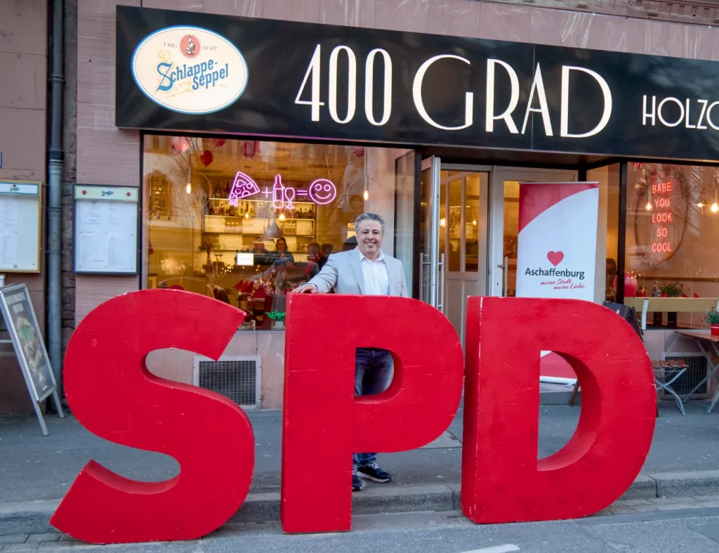 Nach der Wahl ist vor der Wahl. Kassra Adloo vor dem SPD Aufsteller Logo. Foto: Orangeproduction